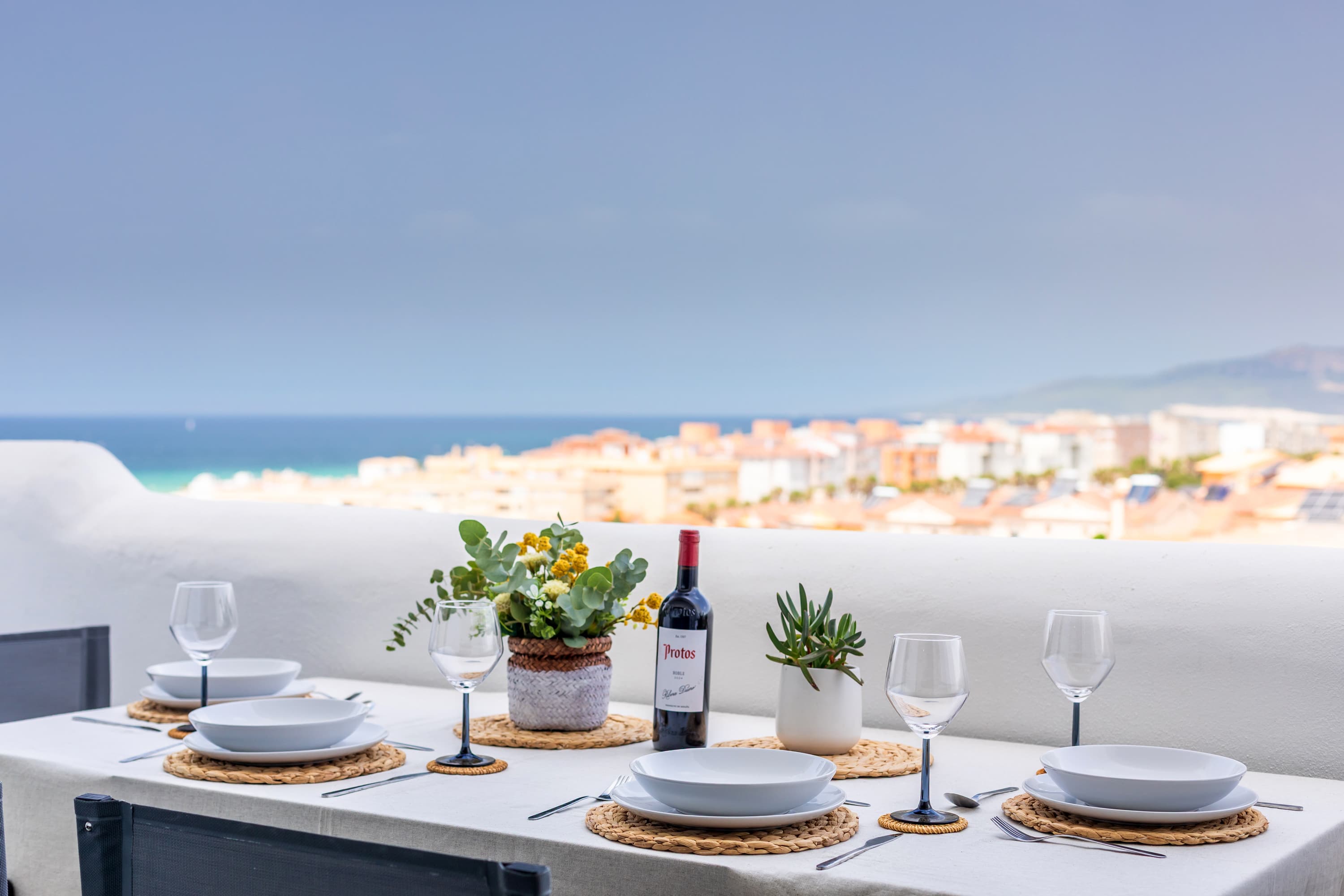 Downstairs Atlantic terrace dining table set for four with wine, flowers, and Bolonia beach stretching to the horizon